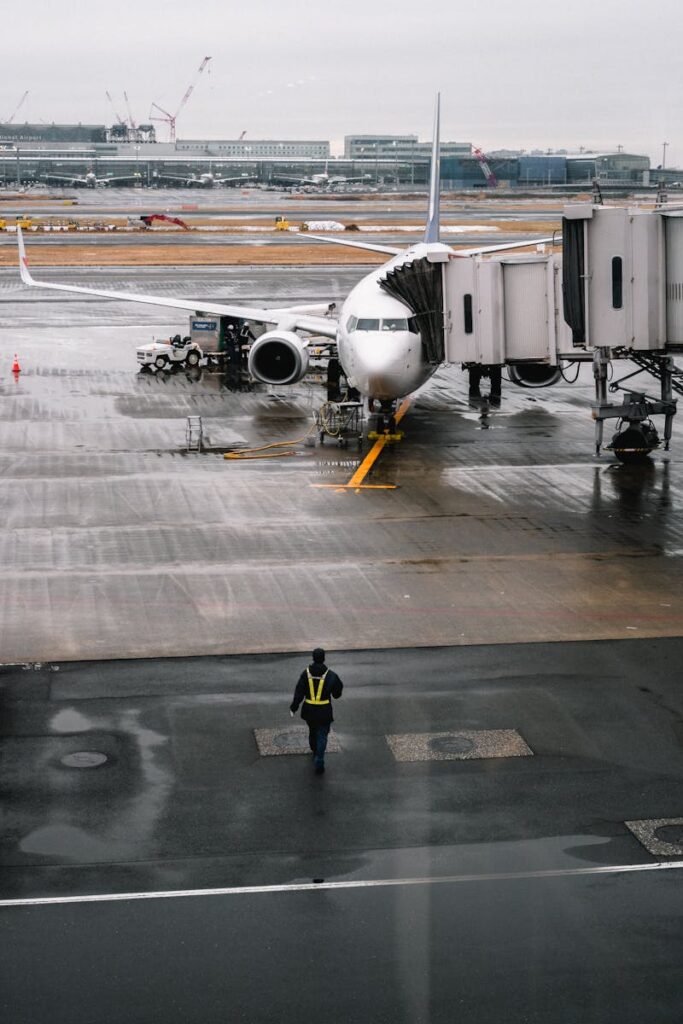 pexels-photo-1928064-1928064 Airplane parked at airport gate on a rainy day with a ground crew member walking.