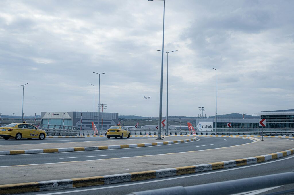 A busy airport scene showing taxi cabs, runway, and an airplane taking off under a cloudy sky.