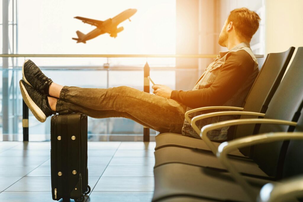 Side view full body of bearded man sitting on chair in waiting hall of airport and looking at flying aircraft and asking if he has enough time for a layover safari at nairobi national park
