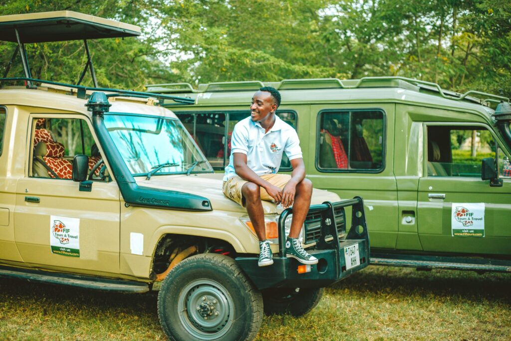 Smiling man seated on safari jeep, ready for Nairobi National Park safari from Nairobi's JKIA Airport excited for the adventure with giraffe nearby.